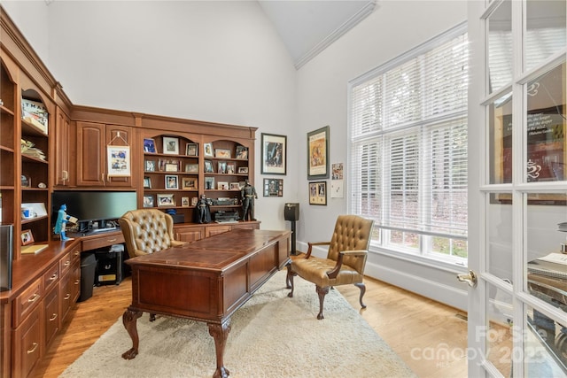 office featuring baseboards, light wood-style floors, ornamental molding, and high vaulted ceiling