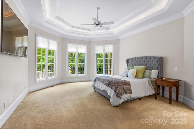 carpeted bedroom with a tray ceiling, multiple windows, baseboards, and ornamental molding