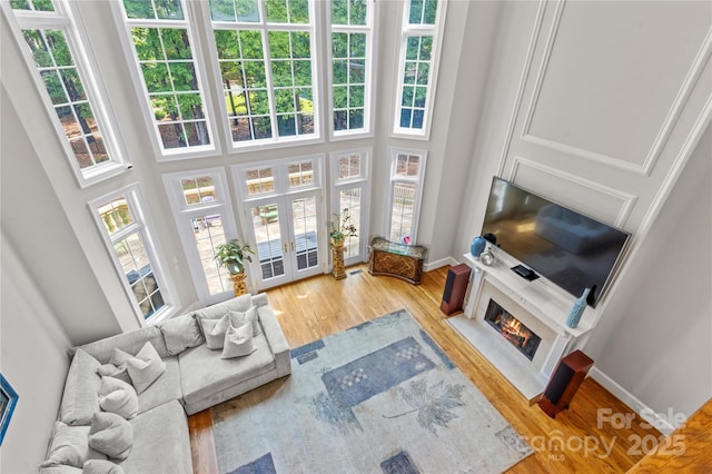 living room featuring a premium fireplace, baseboards, wood finished floors, and a towering ceiling