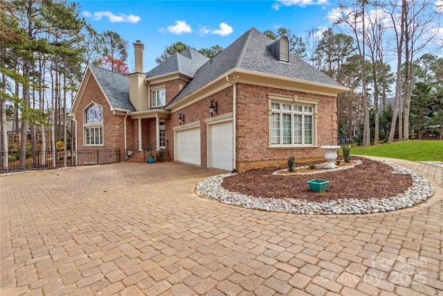 view of front facade featuring decorative driveway, brick siding, a garage, and a chimney