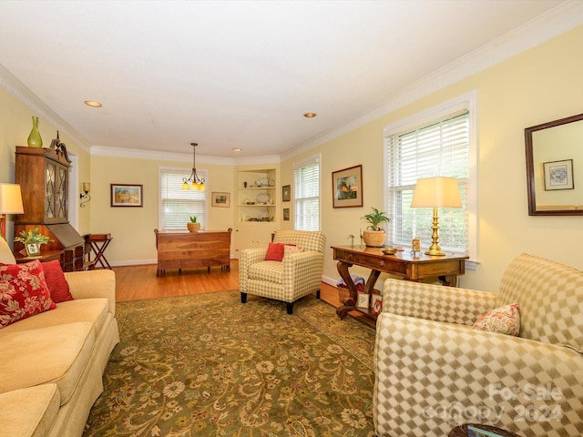 living room featuring built in shelves, wood-type flooring, ornamental molding, and an inviting chandelier