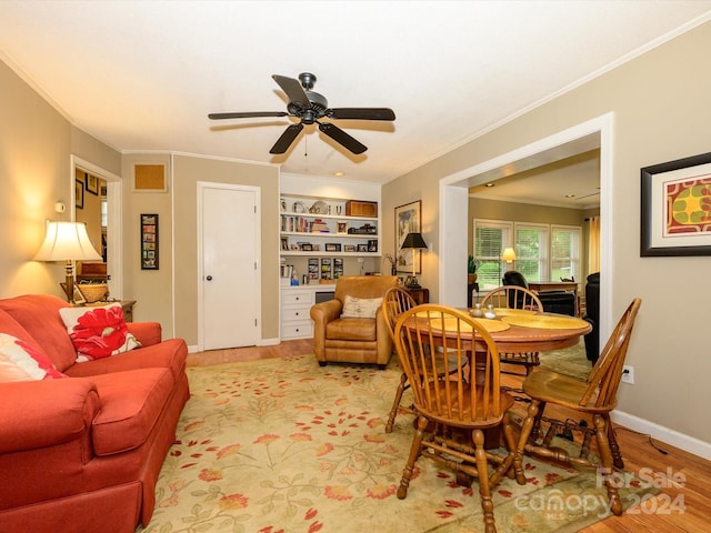 dining room featuring built in shelves, light wood-type flooring, ceiling fan, and crown molding