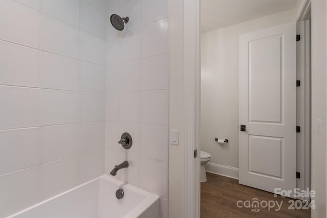 bathroom with hardwood / wood-style floors, toilet, and tiled shower / bath