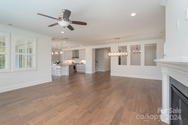 unfurnished living room with ceiling fan with notable chandelier, dark hardwood / wood-style floors, and ornamental molding