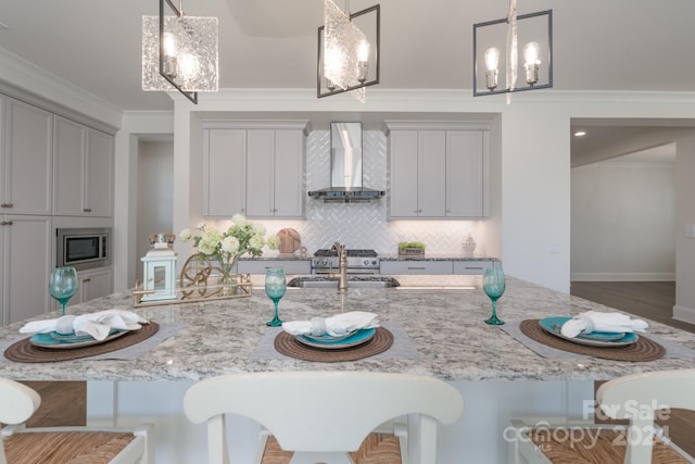 kitchen featuring sink, decorative light fixtures, wall chimney exhaust hood, crown molding, and a kitchen bar