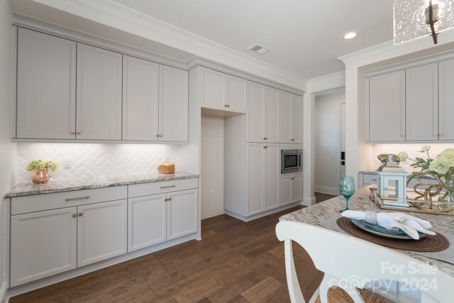 kitchen with ornamental molding, backsplash, light stone countertops, stainless steel microwave, and dark hardwood / wood-style flooring