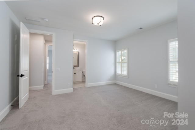 unfurnished bedroom featuring light carpet and ensuite bathroom