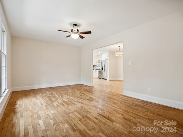 empty room featuring ceiling fan with notable chandelier, light hardwood / wood-style floors, and sink