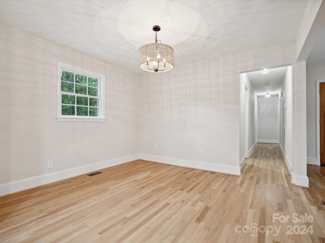 empty room featuring light wood-type flooring and a notable chandelier