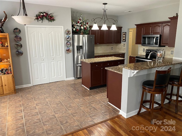 kitchen featuring dark brown cabinets, wood-type flooring, pendant lighting, stainless steel appliances, and dark stone countertops