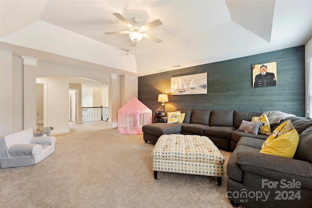 living room with wood walls, ceiling fan, a tray ceiling, and carpet floors