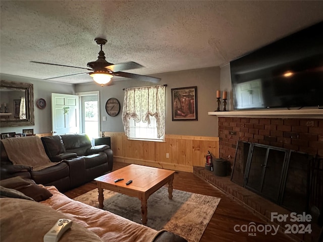 living room with ceiling fan, a textured ceiling, a fireplace, and wooden walls