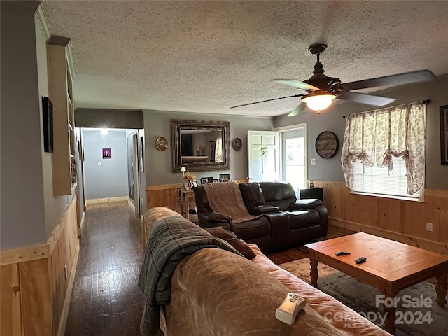 living room with a textured ceiling, wooden walls, dark hardwood / wood-style floors, and ceiling fan