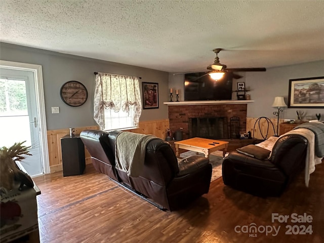 living room featuring wood-type flooring, a textured ceiling, a brick fireplace, wooden walls, and ceiling fan