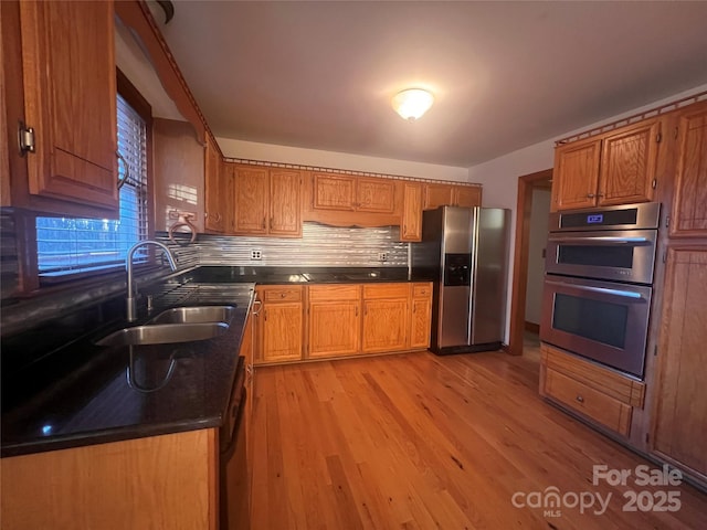 kitchen featuring stainless steel appliances, sink, backsplash, and light hardwood / wood-style flooring