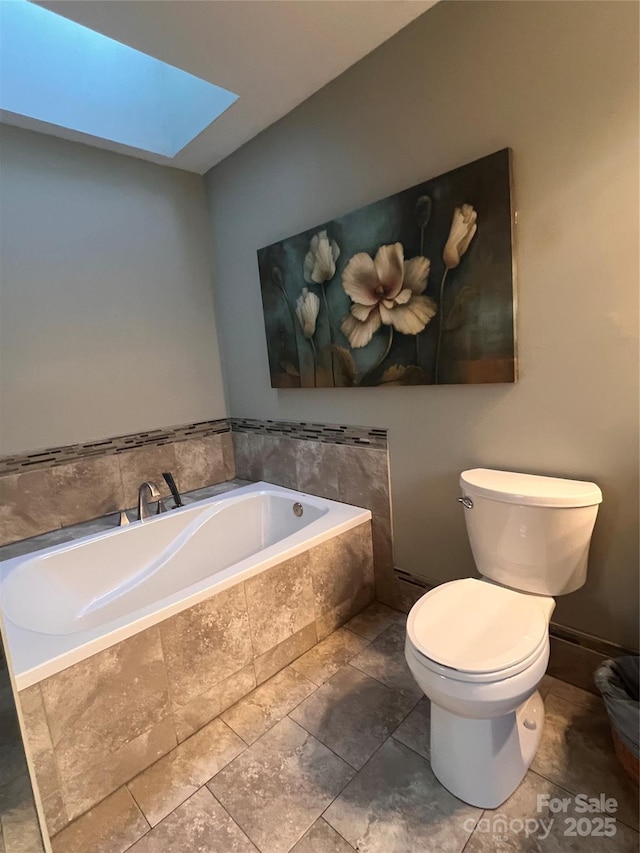 bathroom featuring a relaxing tiled tub, toilet, and a skylight