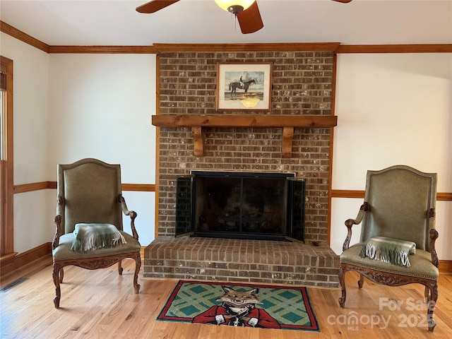 living area featuring hardwood / wood-style flooring, a fireplace, ornamental molding, and ceiling fan