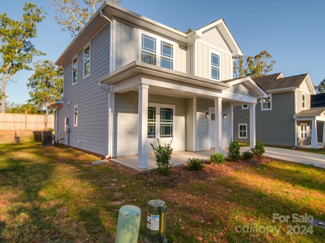 view of front of property with central AC unit, covered porch, fence, board and batten siding, and a front yard