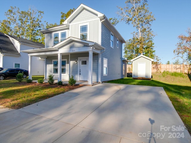 view of front of home with a front lawn, a storage shed, board and batten siding, an outbuilding, and covered porch