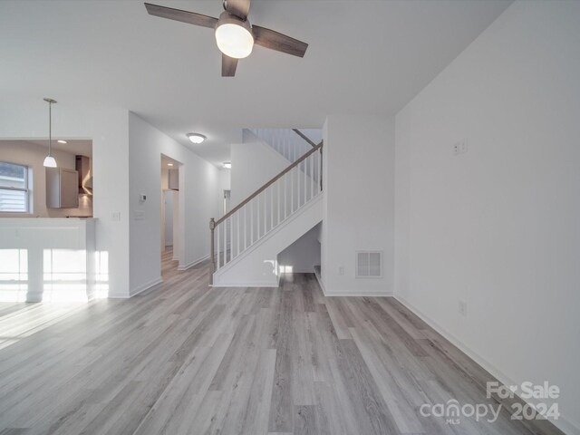 unfurnished living room featuring visible vents, light wood-type flooring, baseboards, stairs, and ceiling fan