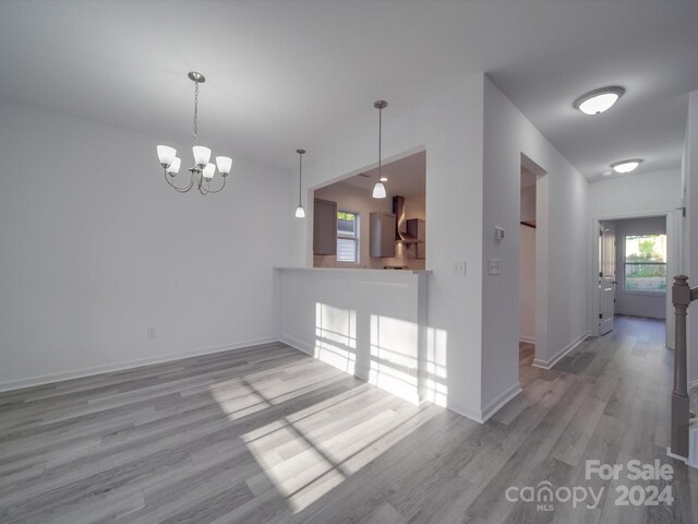 interior space featuring decorative light fixtures, wall chimney range hood, an inviting chandelier, and light wood finished floors