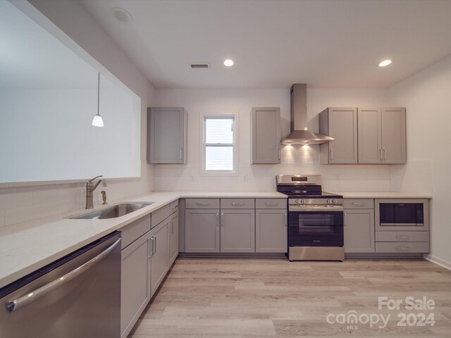 kitchen featuring gray cabinetry, wall chimney exhaust hood, stainless steel appliances, and a sink