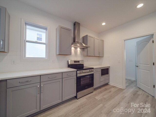 kitchen featuring built in microwave, stainless steel range with electric cooktop, light wood-style floors, wall chimney exhaust hood, and gray cabinetry