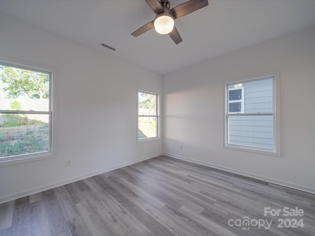 empty room featuring plenty of natural light, visible vents, wood finished floors, and ceiling fan