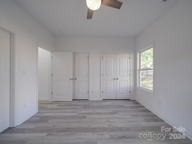 unfurnished bedroom with light wood-style floors, two closets, baseboards, and ceiling fan
