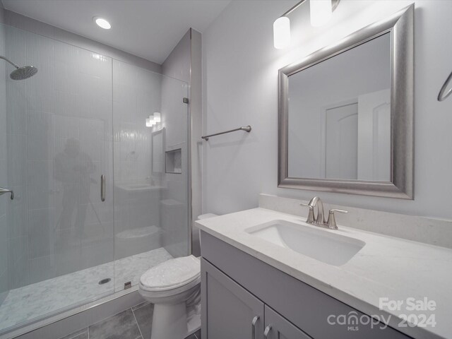 full bathroom with a stall shower, vanity, tile patterned flooring, and toilet