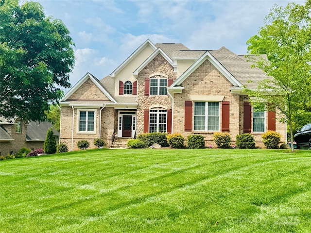 view of front of house featuring brick siding, roof with shingles, stone siding, and a front lawn