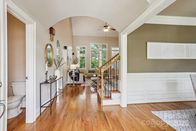 foyer entrance featuring light wood-style flooring, arched walkways, lofted ceiling, stairway, and ceiling fan