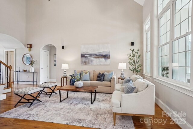 living area with a high ceiling, arched walkways, wood finished floors, and baseboards
