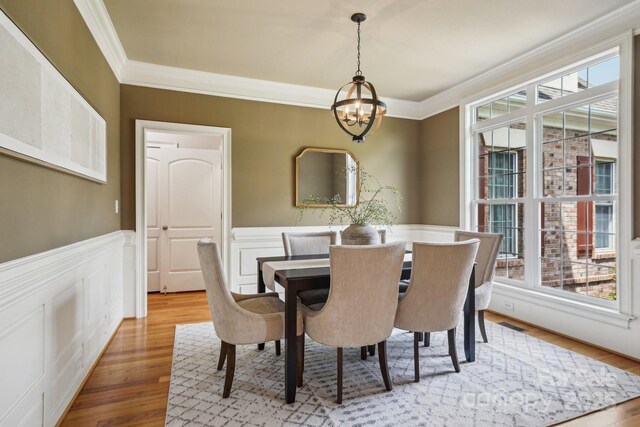 dining area featuring a wealth of natural light, a wainscoted wall, an inviting chandelier, and crown molding