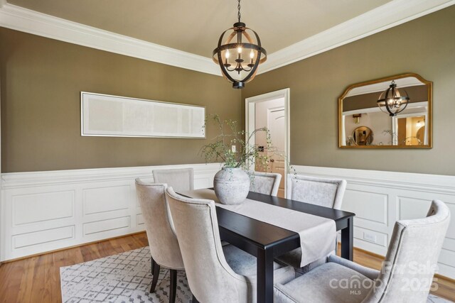 dining area featuring wood finished floors, a chandelier, crown molding, and wainscoting