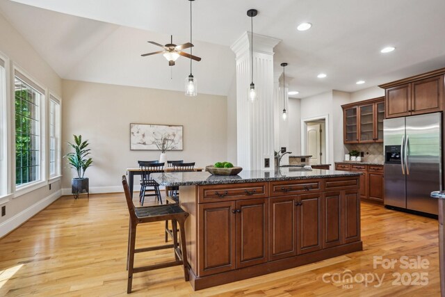 kitchen featuring light wood-style flooring, dark stone counters, stainless steel fridge with ice dispenser, ceiling fan, and a kitchen breakfast bar
