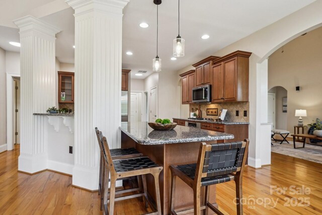 kitchen featuring brown cabinetry, decorative backsplash, light wood-type flooring, stainless steel microwave, and baseboards