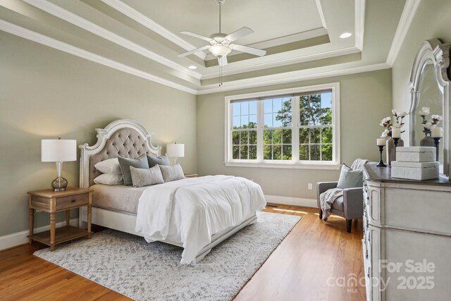 bedroom with baseboards, light wood-type flooring, ornamental molding, and a tray ceiling