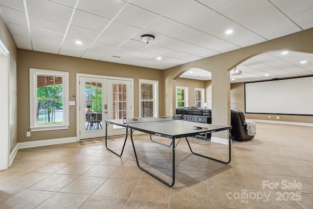 game room featuring light tile patterned flooring, a drop ceiling, arched walkways, french doors, and baseboards