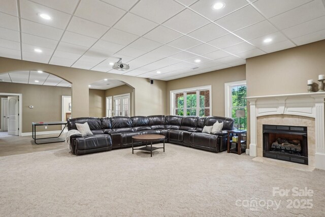 living room with carpet, a tiled fireplace, a paneled ceiling, and arched walkways