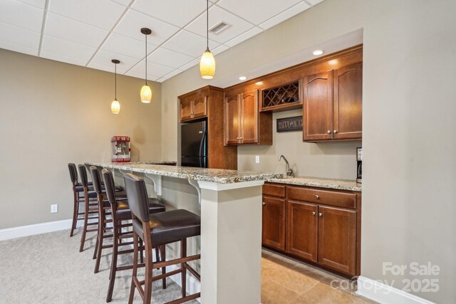 kitchen featuring a kitchen breakfast bar, light stone counters, visible vents, freestanding refrigerator, and a paneled ceiling