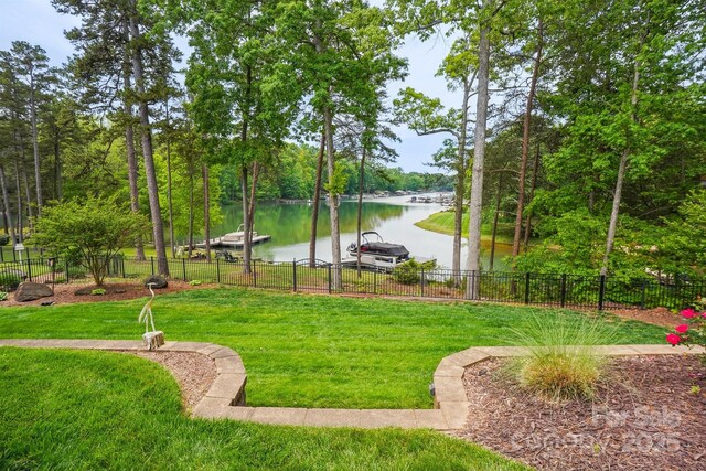 view of home's community with fence, a boat dock, a water view, and a lawn