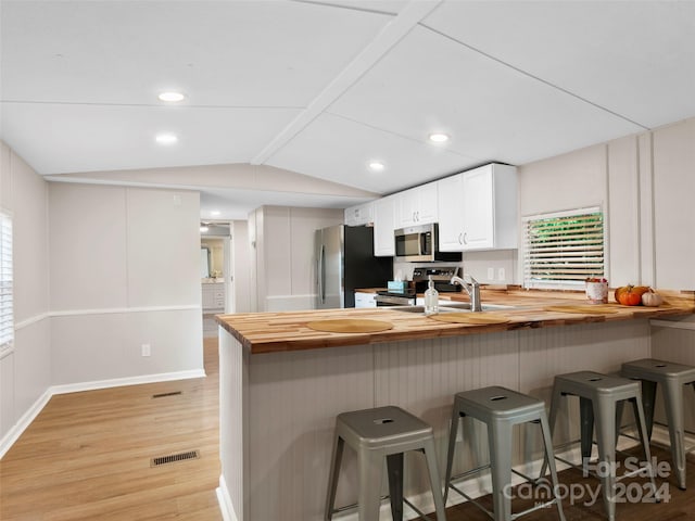 kitchen with stainless steel appliances, white cabinets, plenty of natural light, and vaulted ceiling