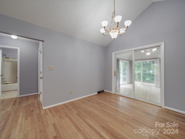 empty room featuring high vaulted ceiling, light wood-type flooring, a chandelier, and a textured ceiling