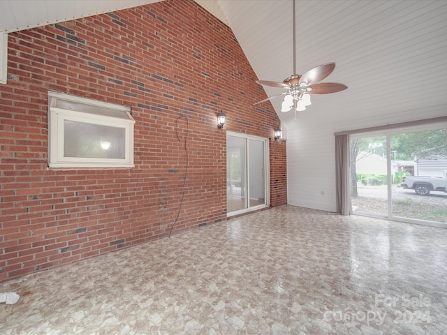 unfurnished room featuring high vaulted ceiling, ceiling fan, and brick wall