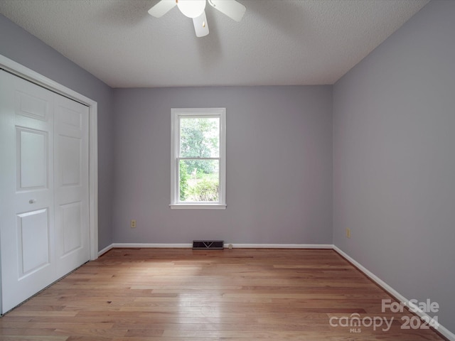 unfurnished bedroom with a closet, ceiling fan, light wood-type flooring, and a textured ceiling