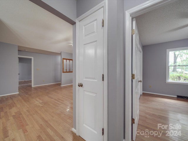 hall featuring light wood-type flooring and a textured ceiling