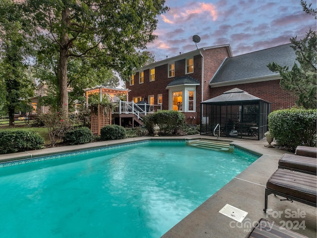 pool at dusk with a deck and a gazebo