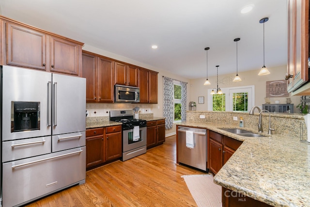 kitchen with pendant lighting, appliances with stainless steel finishes, sink, and light stone counters