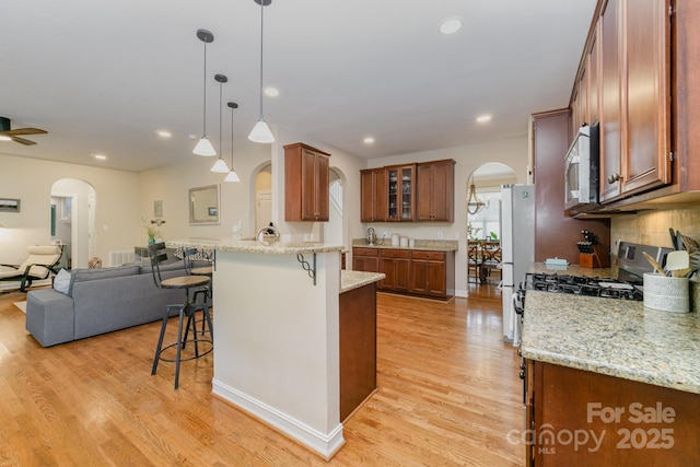 kitchen featuring appliances with stainless steel finishes, a breakfast bar, pendant lighting, light stone counters, and light wood-type flooring